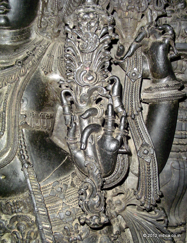 Hoysala Art. It appears as executed in cast metal. In fact this is carved out of soft soapstone, and  hardened over a period. The softer soapstone is highly workable, especially for the finer details. This is the image of the door keeper deity at Chennakeshava temple in Belur, Karnataka.  